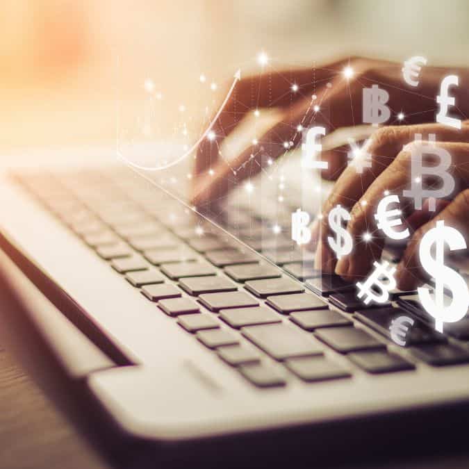 Hands typing on a laptop with floating currency symbols representing digital products to sell and global online business opportunities.