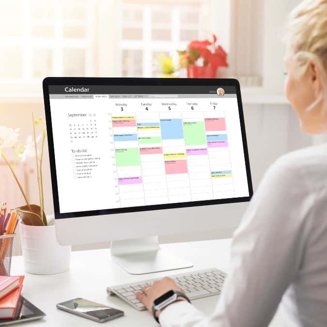 Person viewing a digital calendar planner on a computer screen, with a color-coded weekly schedule, representing popular digital planners to sell on Etsy.