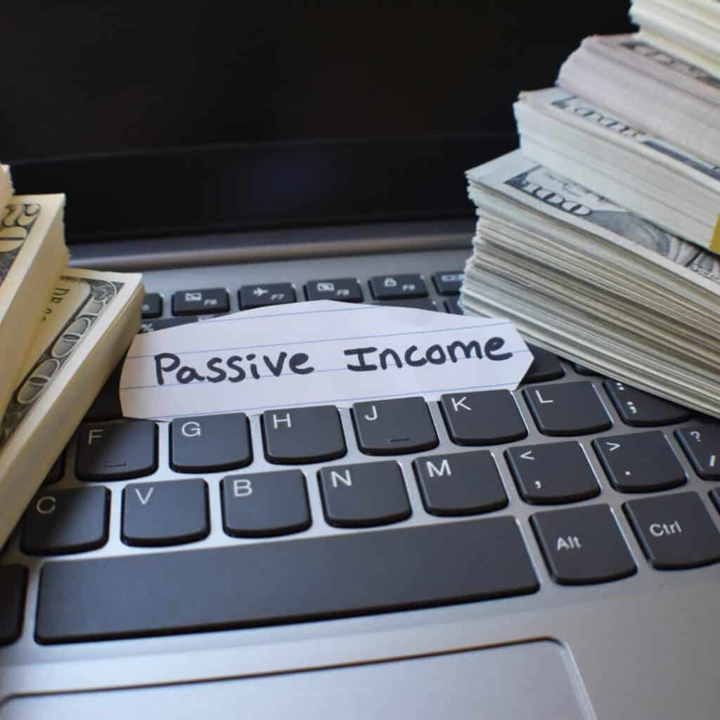 Stacks of cash labeled "Passive Income" on a laptop keyboard, representing earnings from digital products as a side hustle.